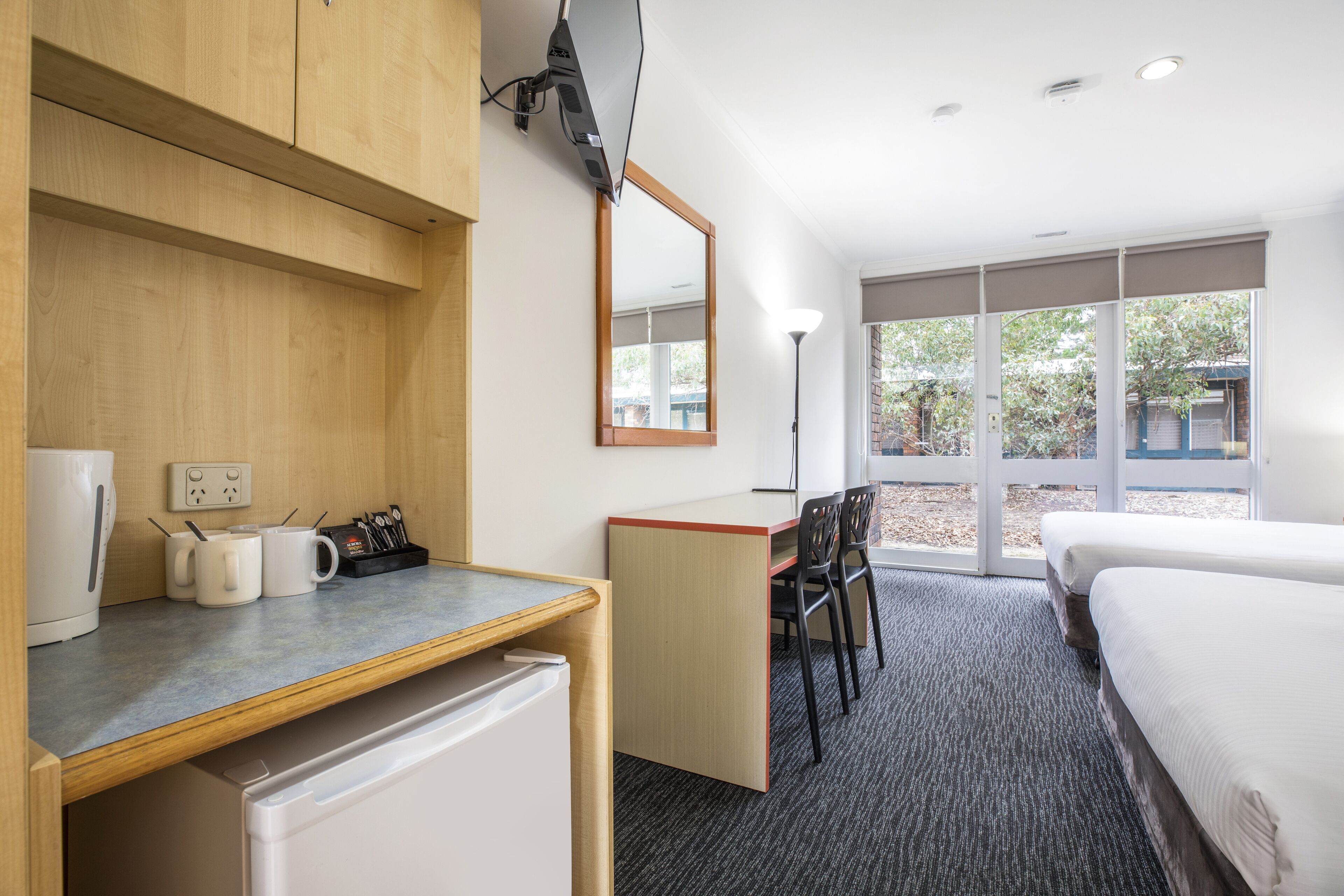 Una habitación de hotel con kitchenette, un escritorio con silla, una cama y ventanas amplias.