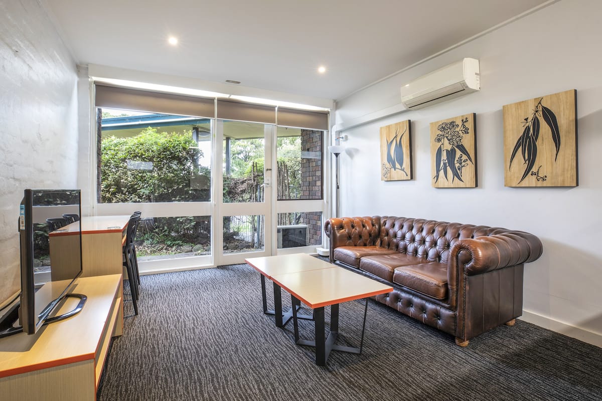 Un espace de bureau moderne avec un canapé en cuir, un bureau et une grande fenêtre donnant sur un paysage verdoyant.