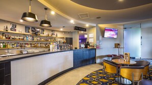 Zona de recepción de hotel con bar, área de descanso y una pantalla de televisión.