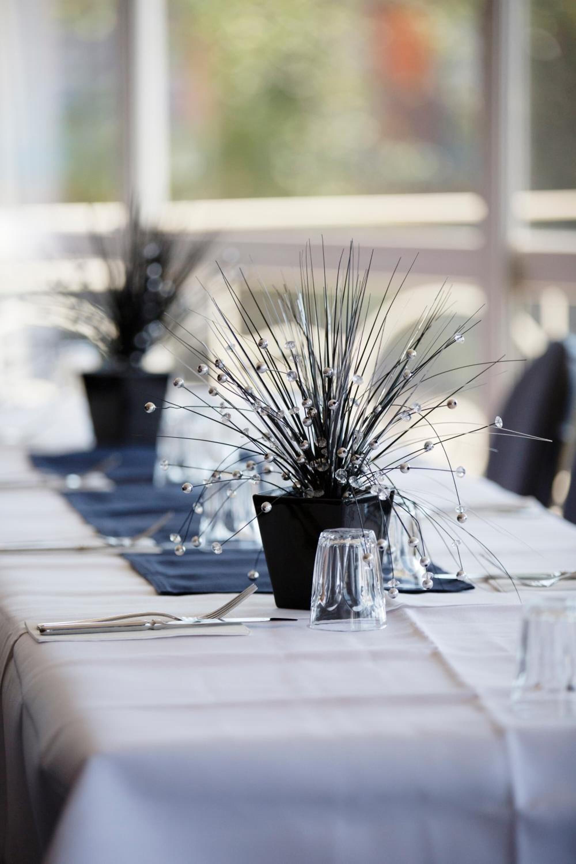 A dining table set with a clear glass vase, a black pot with a plant, and a fork.