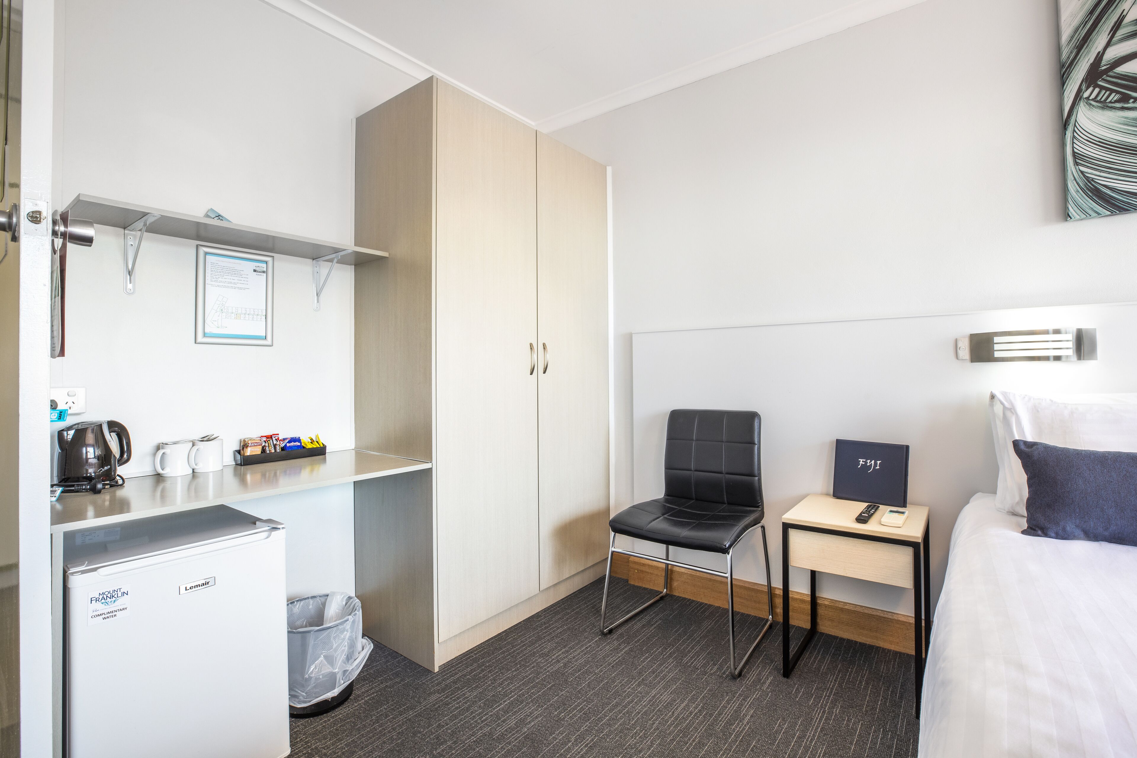 Ein Hotelzimmer mit Bett, Schreibtisch mit Stuhl, Minibar, Mülleimer und Kleiderschrank.