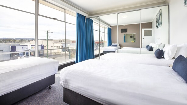 Habitación de hotel con dos camas, ventanas amplias y vistas a la ciudad.