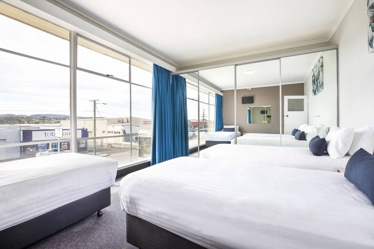 A hotel room with two beds, large windows, and a view of the city.