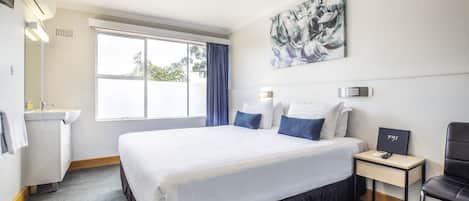 Camera d'albergo con un letto grande, un comodino con telefono e un cartello, una scrivania, una sedia, una finestra con tende, un lavandino e uno specchio.