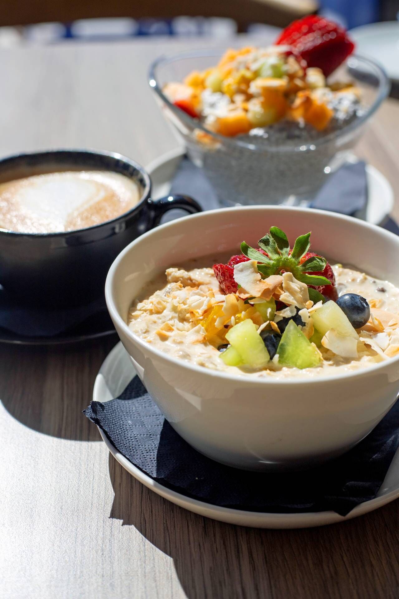 A bowl of oatmeal topped with fruits and nuts, a cup of coffee, and a glass of orange juice on a wooden table.