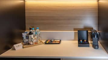 A compact kitchen area with a countertop, a coffee machine, a wine glass, and a small refrigerator.