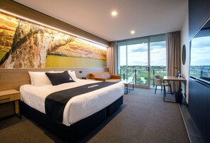 Habitación de hotel moderna con una cama grande, un escritorio y vistas a un puente y al paisaje a través de amplios ventanales.