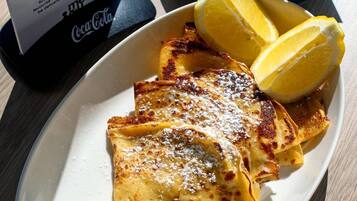 Un plat de crepes amb sucre glas i aranyons blaus, una tassa de cafè i un objecte de Coca-Cola.