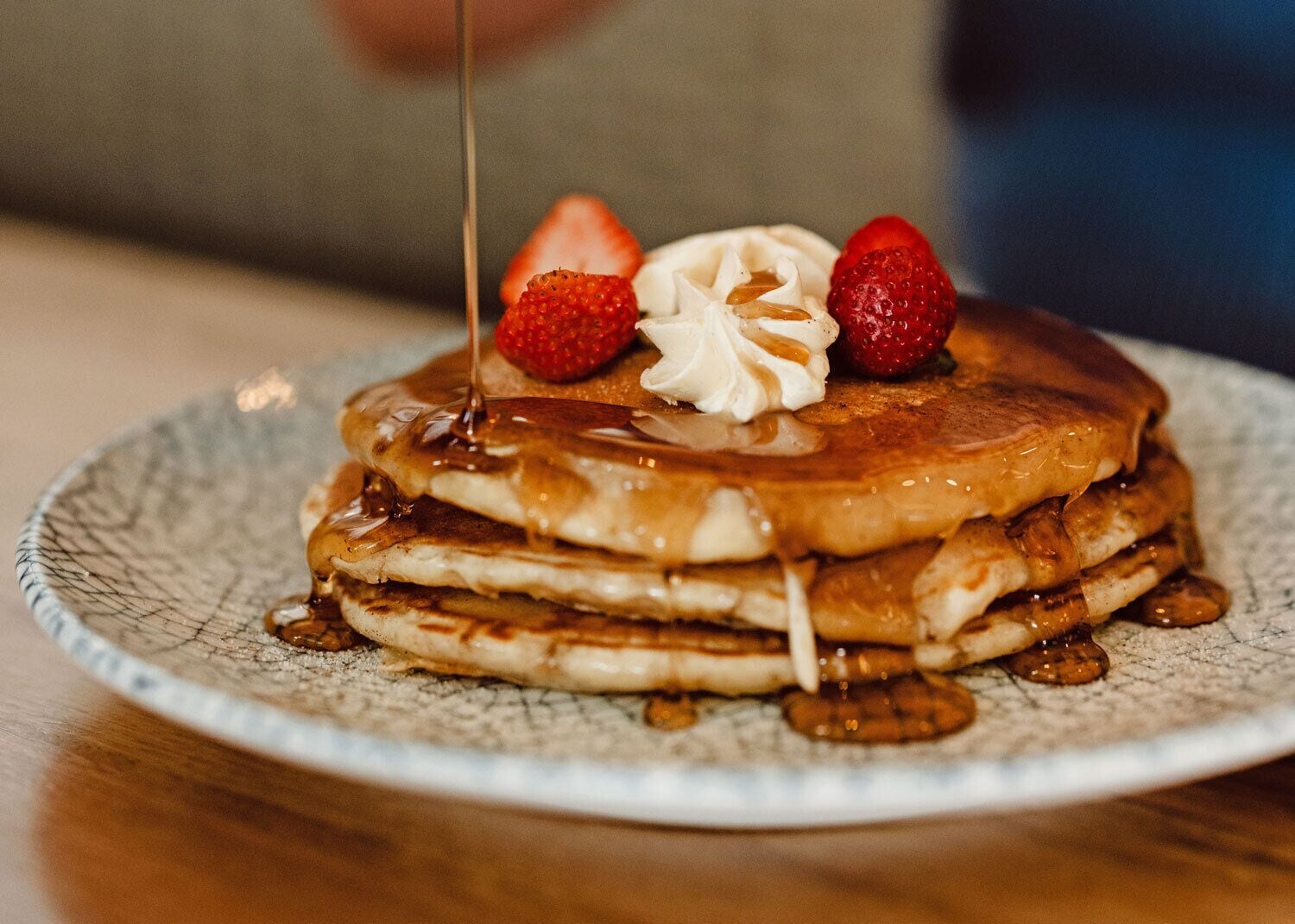 A stack of pancakes with syrup and strawberries on a ceramic plate.