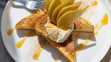 A plate with a dessert consisting of a slice of cake topped with whipped cream and apple slices, drizzled with syrup.