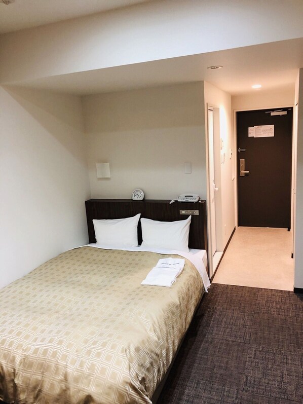 Une chambre d’hôtel avec un lit, un réveil, un téléphone et une porte avec une pancarte.
