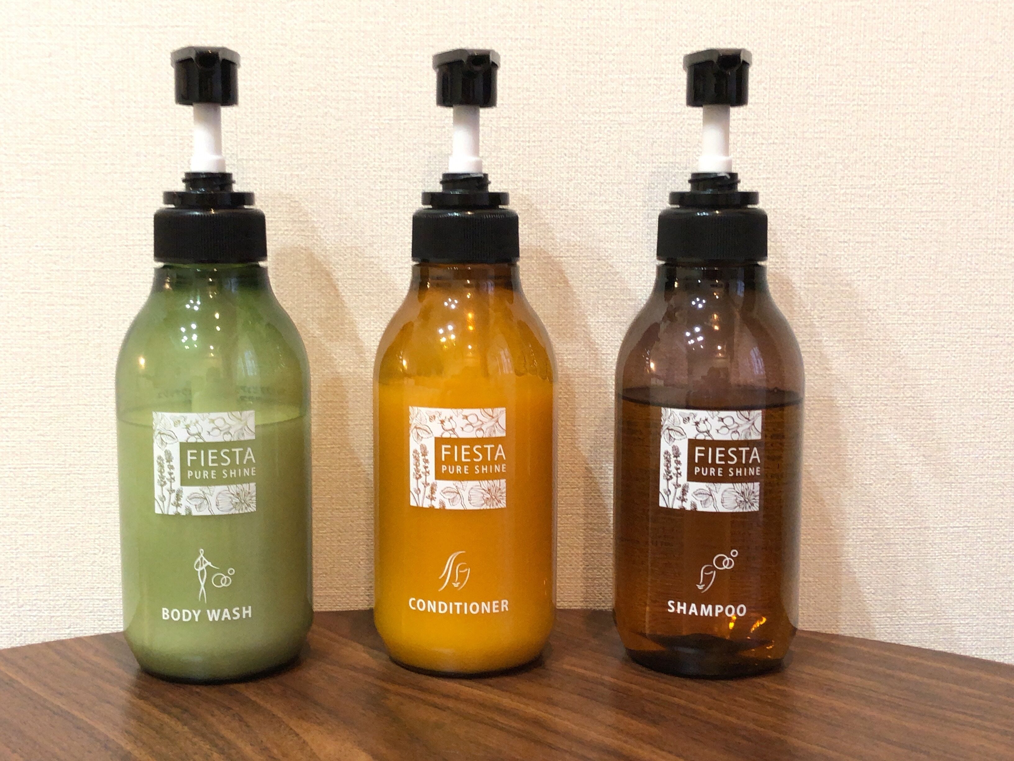 Três frascos de Fiesta Pure Shine com shampoo, condicionador e líquido de banho sobre uma superfície de madeira.