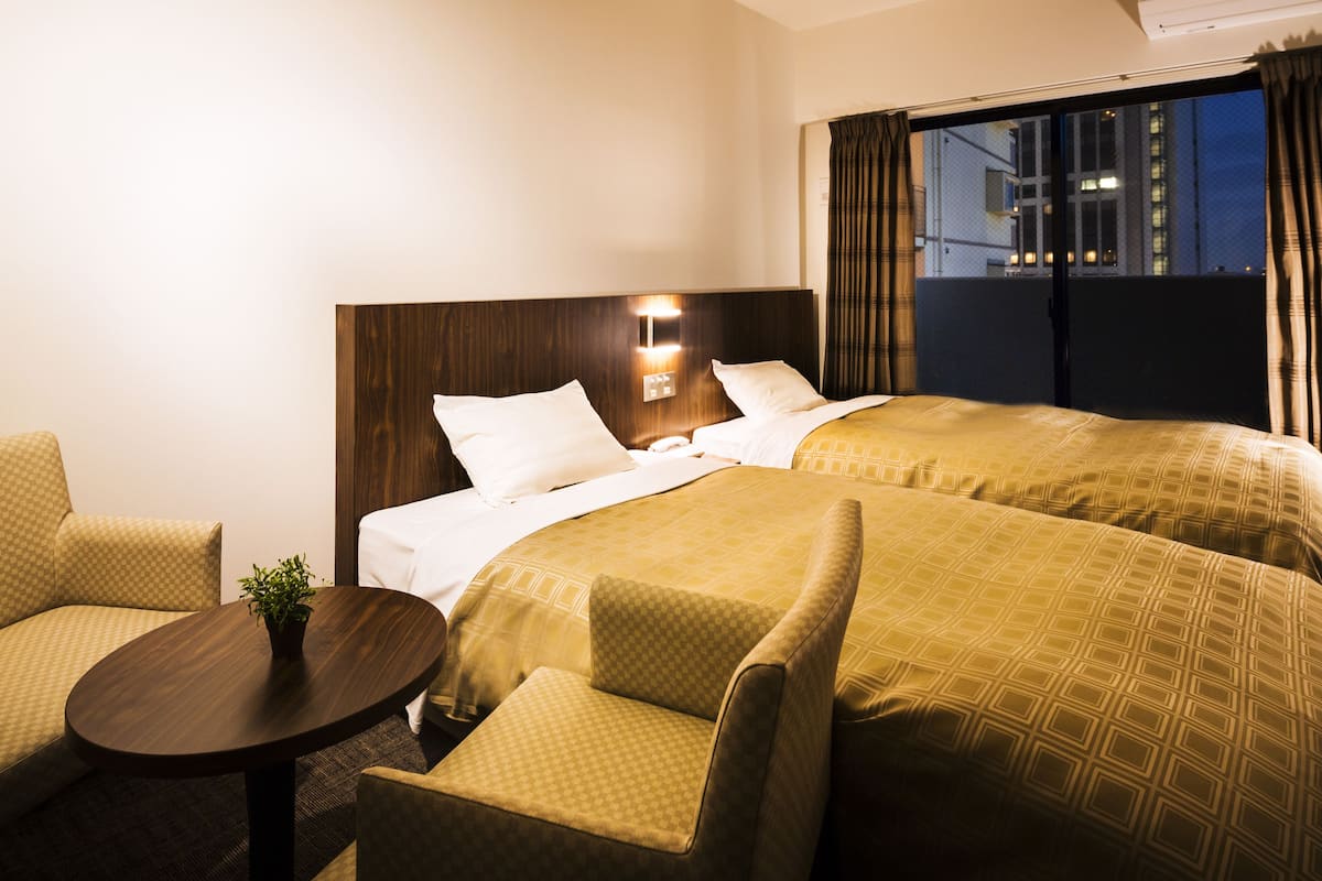 Quarto de hotel com duas camas, uma mesinha com uma planta e um sofá.