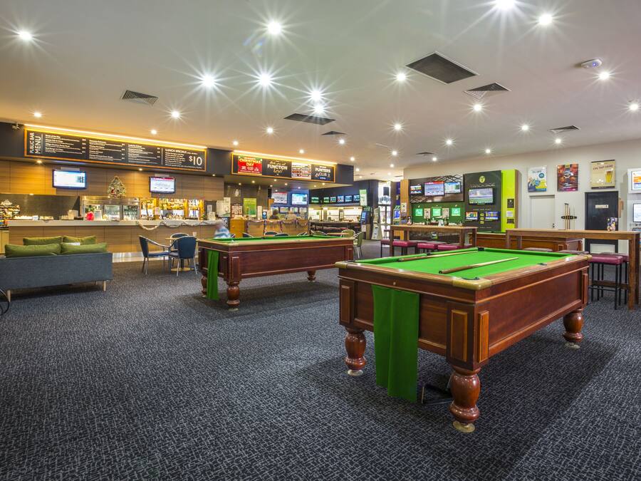 A pool hall with multiple pool tables, a bar area, and a menu board.