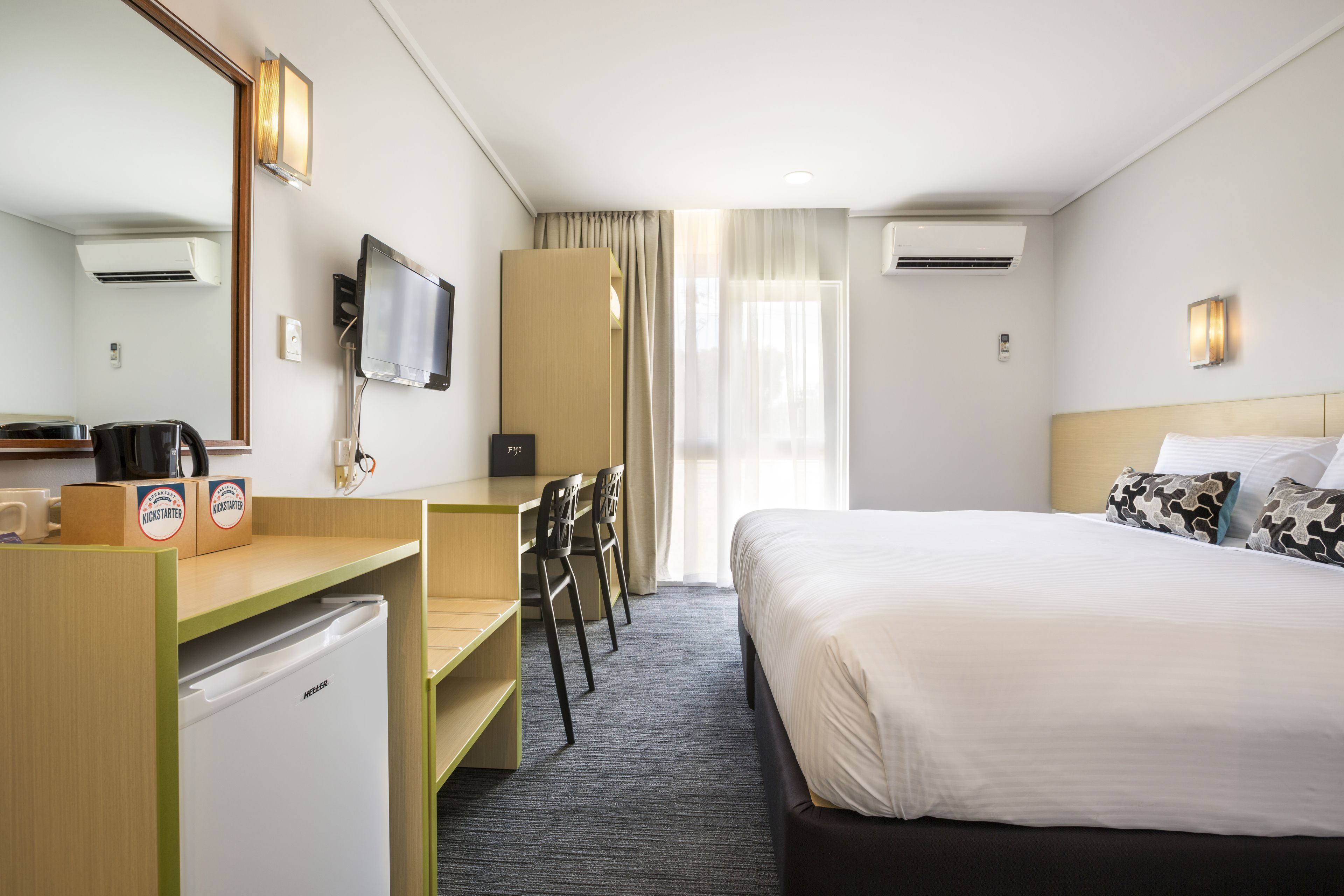 Ein Hotelzimmer mit Bett, Schreibtisch, Stühlen, Fernseher und Minibar.