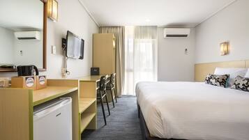 Ein Hotelzimmer mit Bett, Schreibtisch, Stühlen, Fernseher und Minibar.