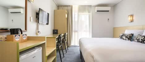 A hotel room with a bed, desk, chairs, a television, and a minibar.