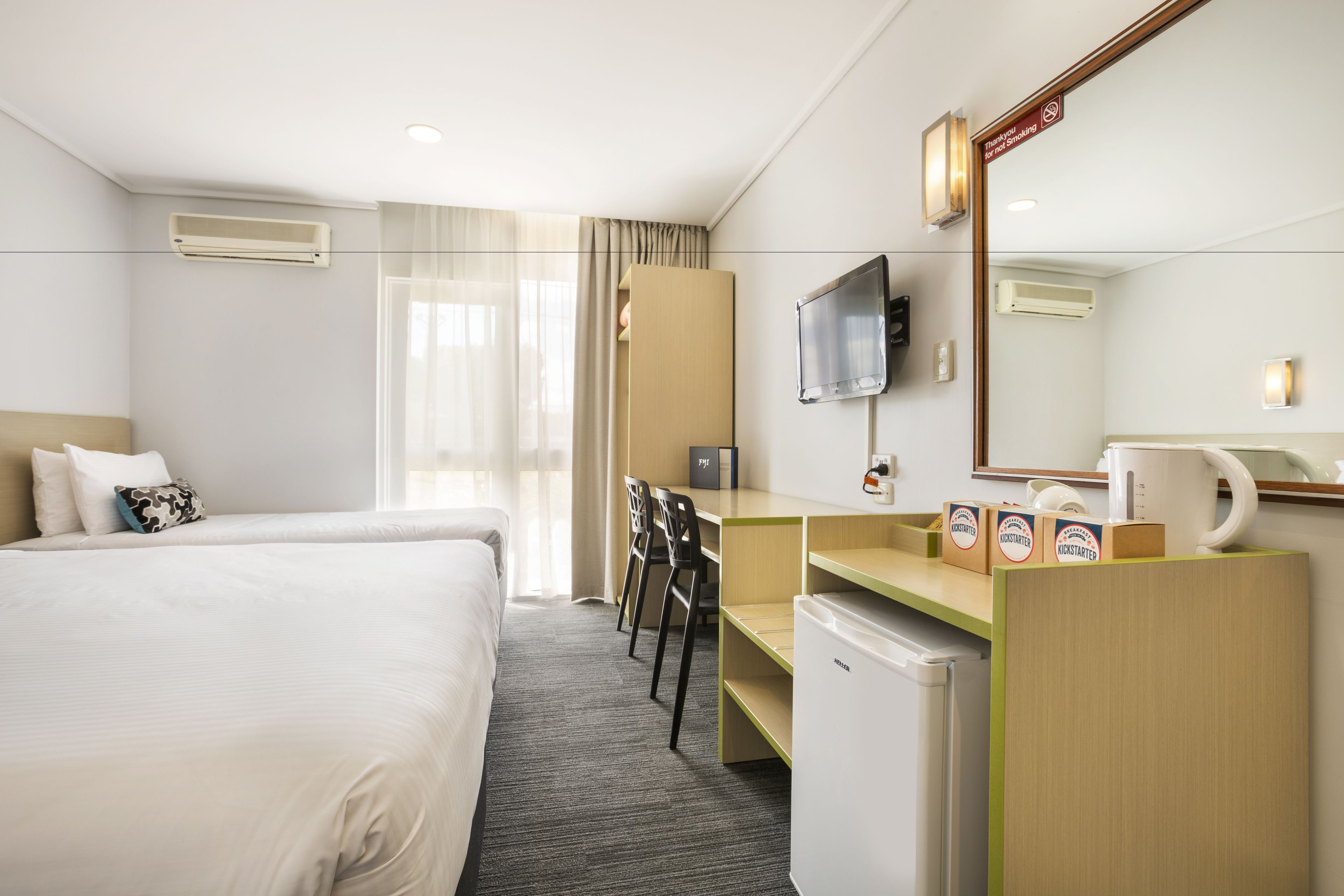 A hotel room with a bed, a desk, two chairs, a television, a coffee maker, and a minibar.