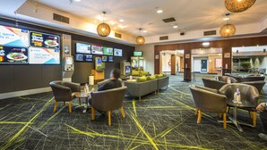 A hotel lobby with seating areas, a food service counter, and a large screen displaying information. - Nightcap at Coolaroo Hotel (Coolaroo)