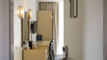 Quarto de hotel com escrivaninha, cadeiras, televisão, minibar e um espelho grande.