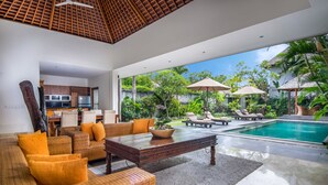 Ampla sala de estar com um sofá grande, uma mesa de centro e vista para uma piscina e um jardim exuberante.