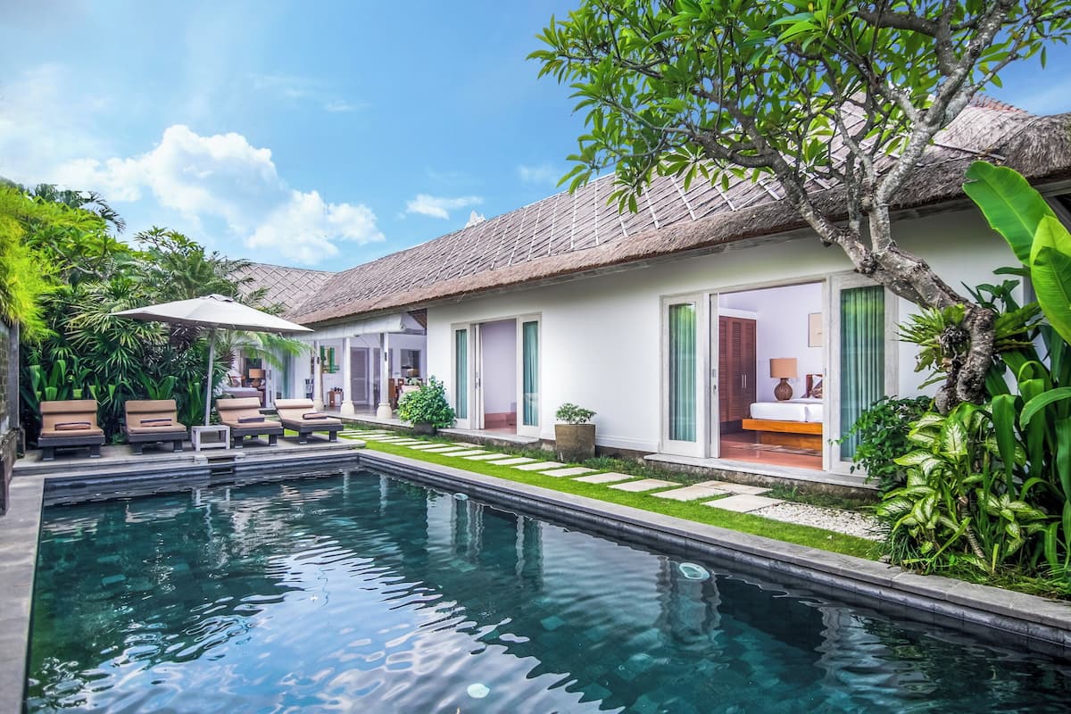 A pool area with lounge chairs and a thatched-roof building.