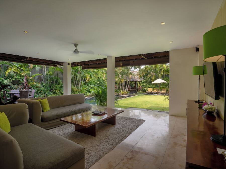 Amplia sala de estar con sofá, mesa de centro y vistas a un jardín exuberante a través de grandes ventanales.