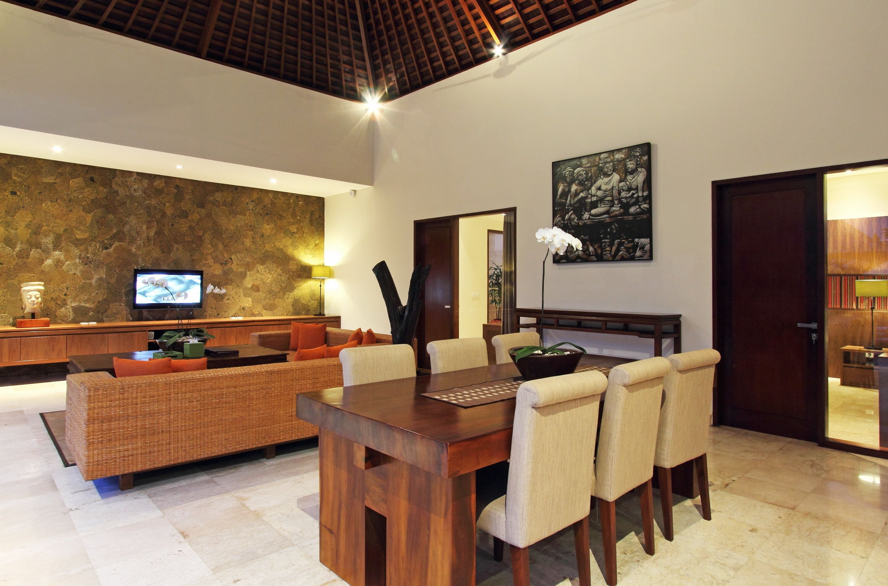 Un amplio salón con una mesa y sillas de madera, un sofá, un televisor y una pared de piedra.
