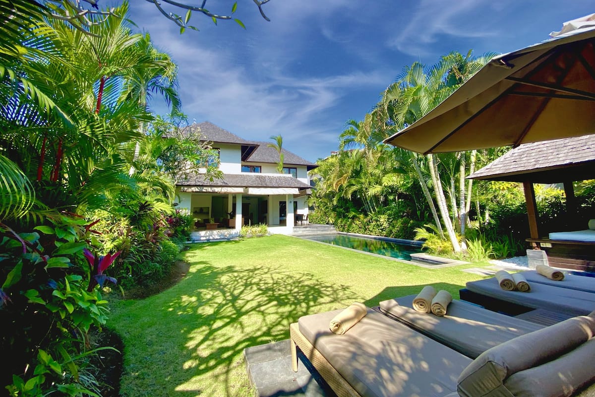 A tropical resort with a swimming pool, lounge chairs, and lush greenery.