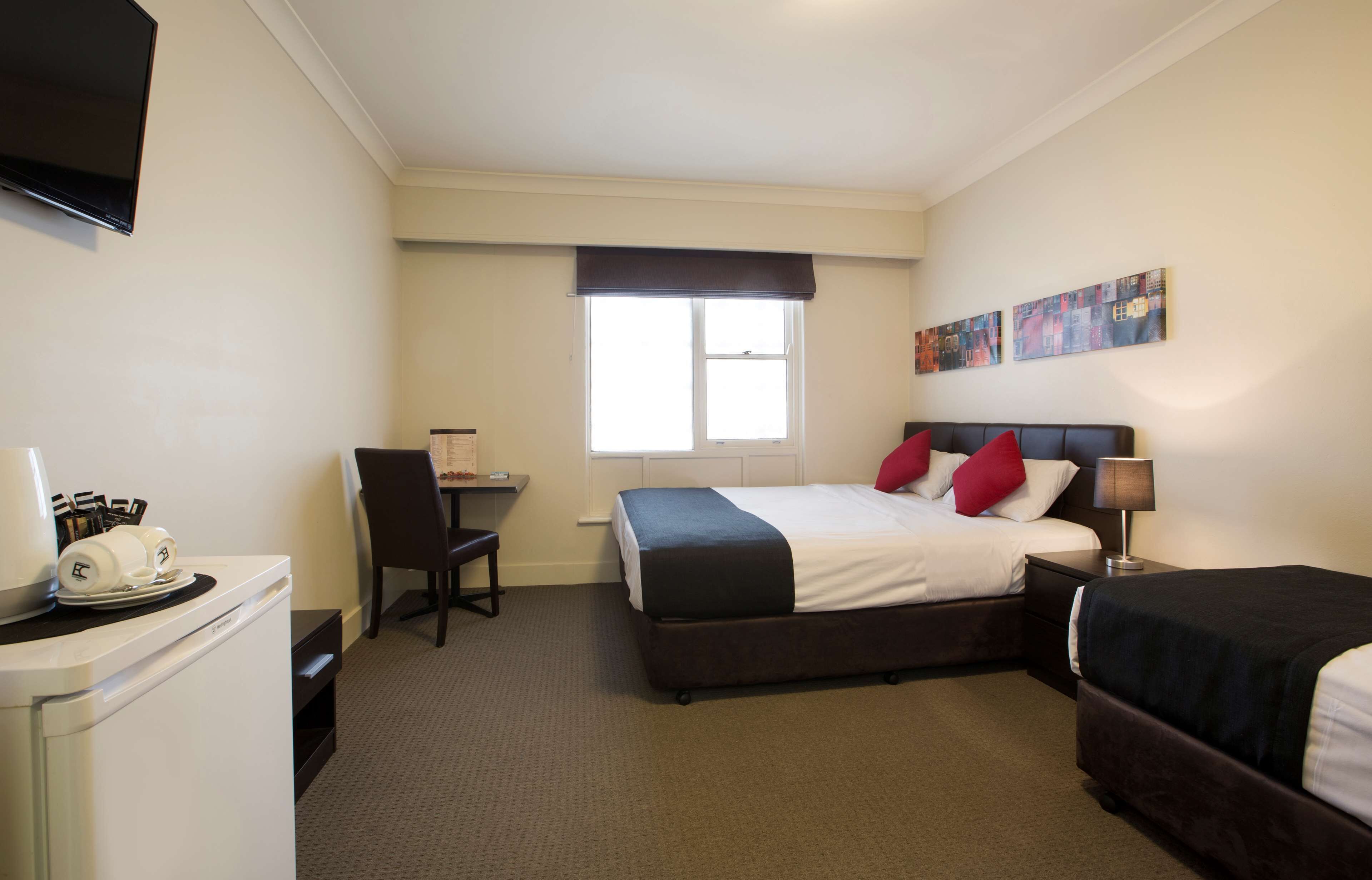 A hotel room with a bed, a desk, a chair, a TV, and artwork on the wall.