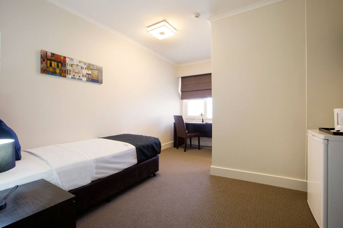 A hotel room with a bed, a desk, a chair, and a small refrigerator.