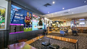 A sports bar with a large screen displaying rugby matches, bar area, seating, and a counter. - Nightcap at Excelsior Hotel (Thomastown)