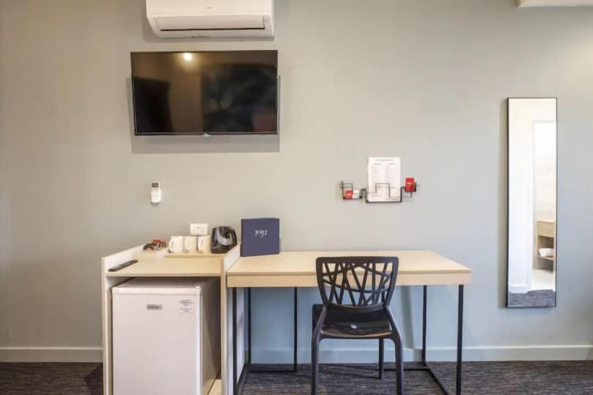 Habitación de hotel con escritorio, silla, refrigerador, televisor de pantalla plana y espejo.