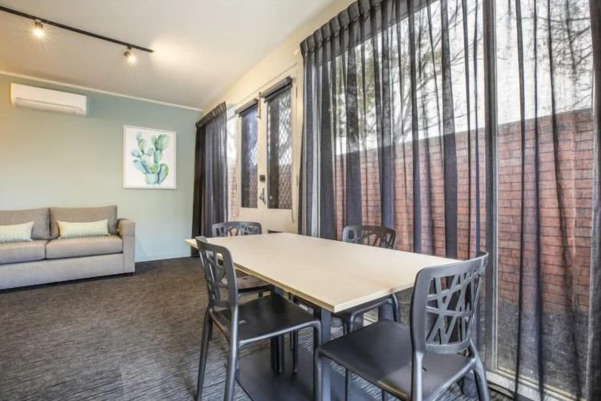 Un área de comedor con una mesa y sillas, un sofá y una ventana con cortinas.