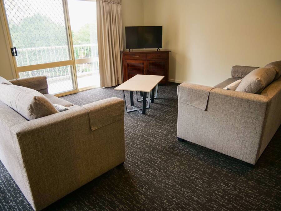 Une chambre d’hôtel avec deux canapés, une petite table, un téléviseur posé sur un meuble et une grande fenêtre donnant sur un paysage verdoyant.