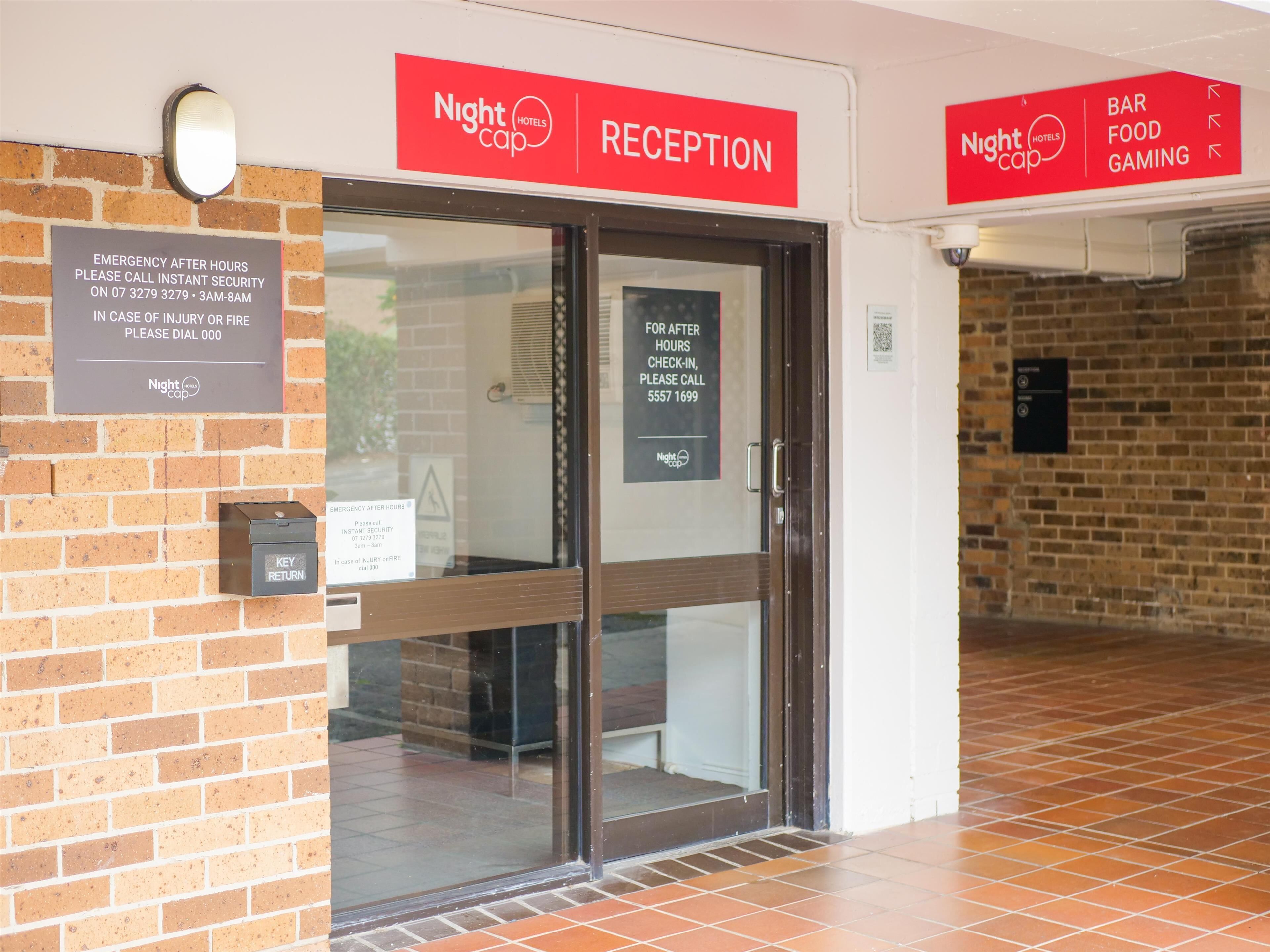 A hotel reception area with a glass door, emergency contact information, and signs for the reception and bar food gaming.