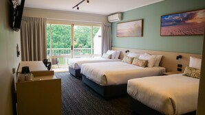 Habitación de hotel con dos camas, un escritorio, una silla y un balcón con vistas a la vegetación.