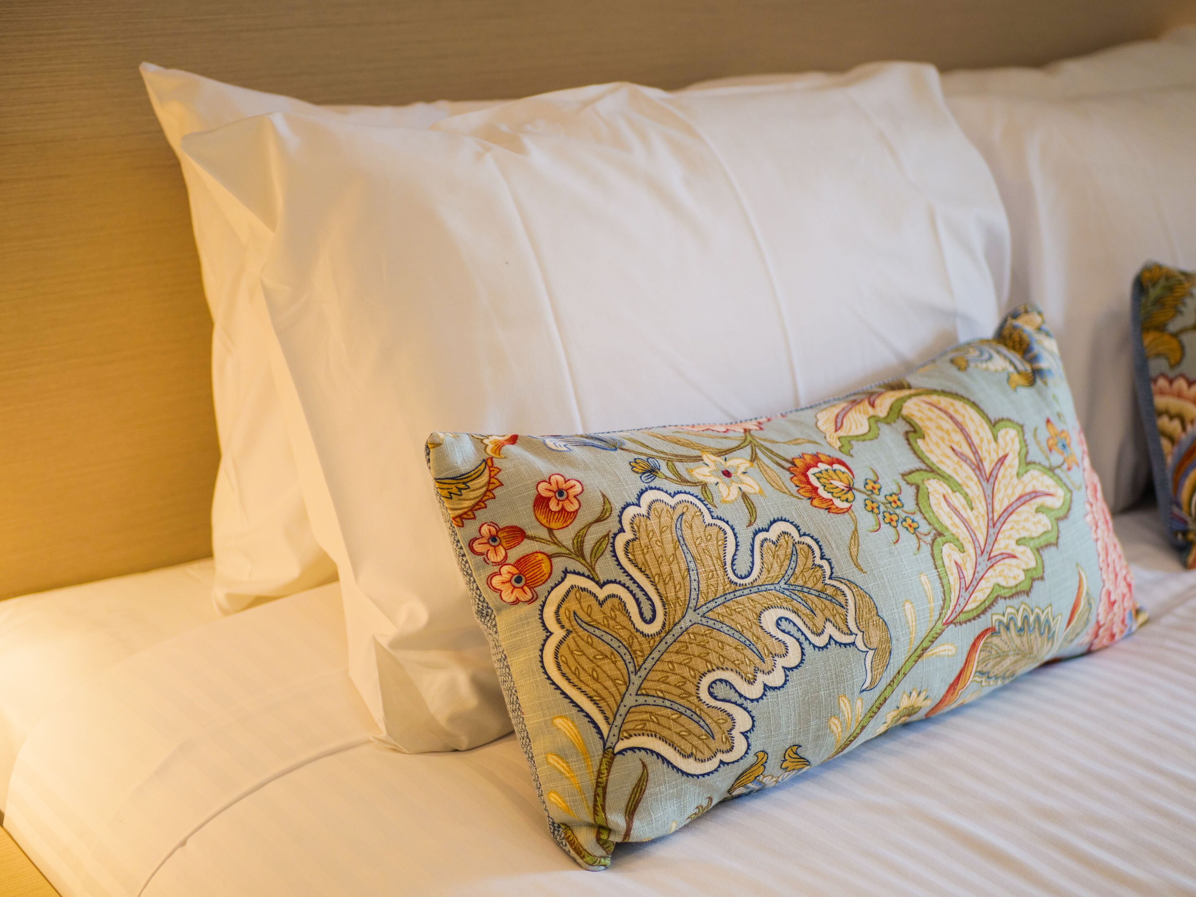 A bed with white pillows and a colorful embroidered pillow.
