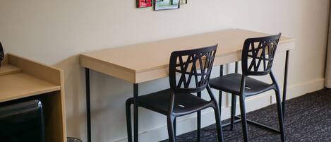 A small room with a wooden desk and two black chairs. There is a trash can and a wall-mounted menu.