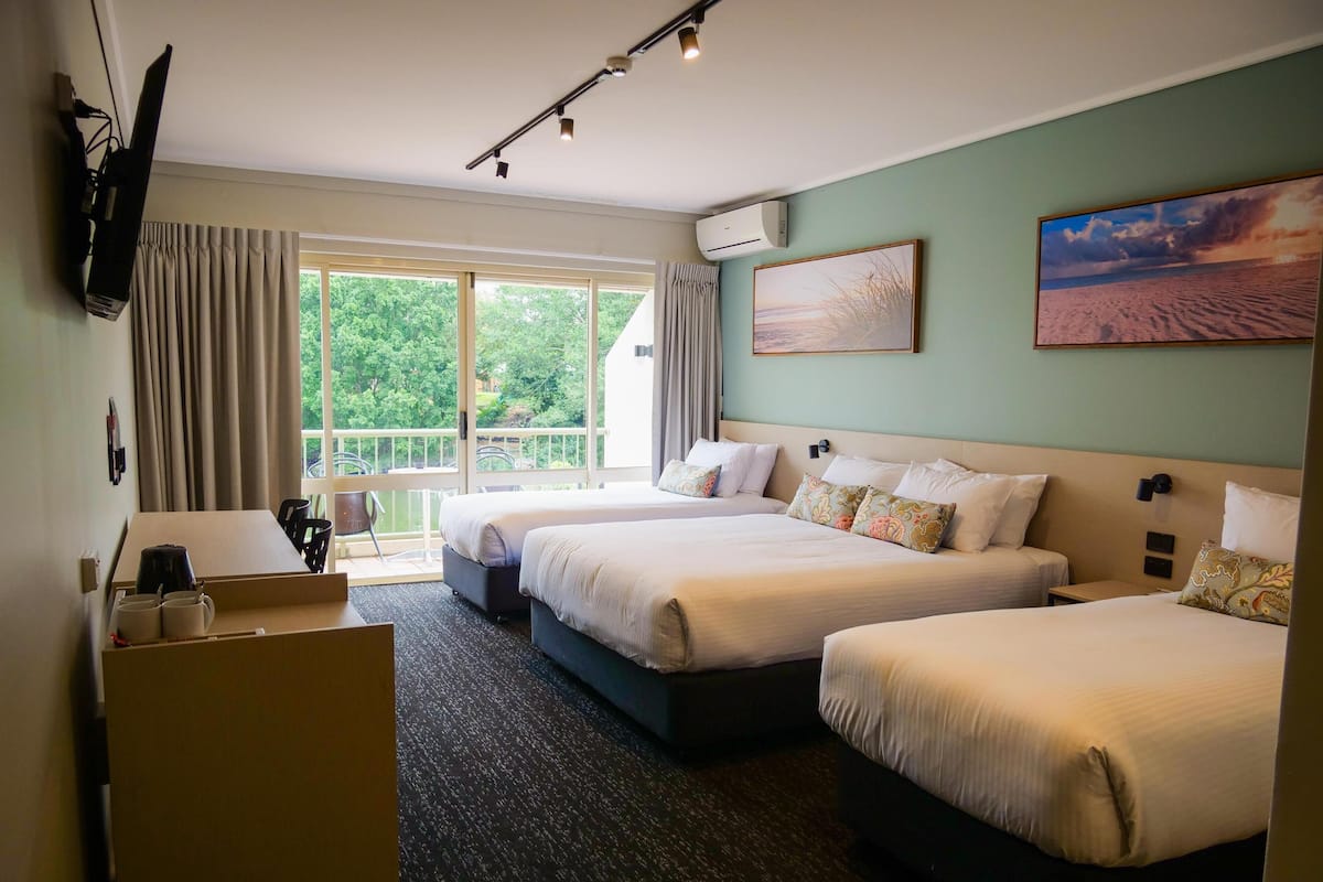 Una habitación de hotel con dos camas, un escritorio con cafetera y un balcón con cortinas.
