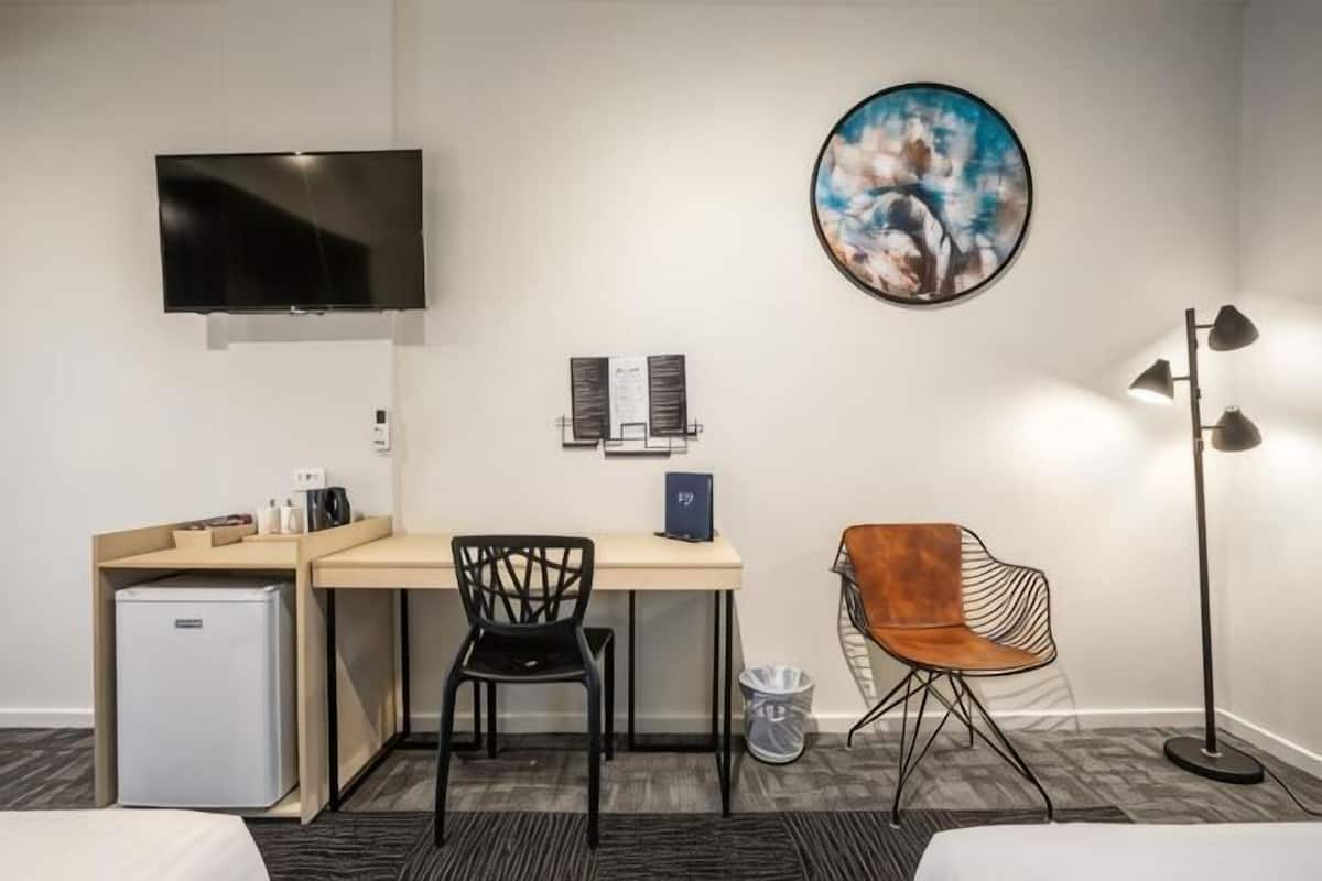 Une chambre d’hôtel équipée d’un bureau, de deux chaises, d’une télévision, d’un tableau et d’une lampe sur pied.