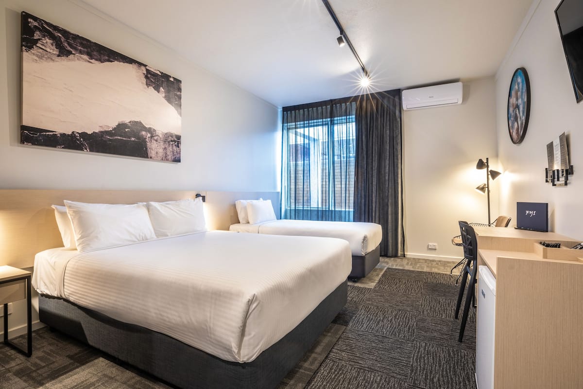 Une chambre d’hôtel avec deux lits, un bureau et un grand tableau au mur.