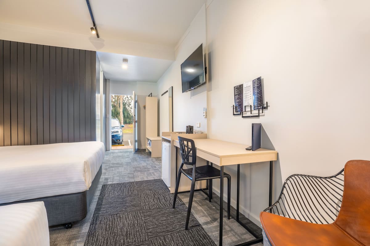 Une chambre d’hôtel équipée d’un lit, d’un bureau, d’une chaise et d’un téléviseur fixé au mur.