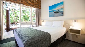 Ein Hotelzimmer mit einem großen Bett, einem Fenster mit Blick auf Grünflächen, einem Bild mit Strandmotiv und einem Nachttisch mit Telefon.