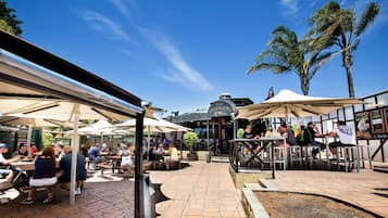Un espace extérieur aménagé en terrasse avec des tables et des parasols, une enseigne indiquant « The Swinging Pig », et des palmiers en arrière-plan.