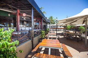 An outdoor patio area with wooden tables and benches, a covered seating area, and a bar with a Guinness sign.