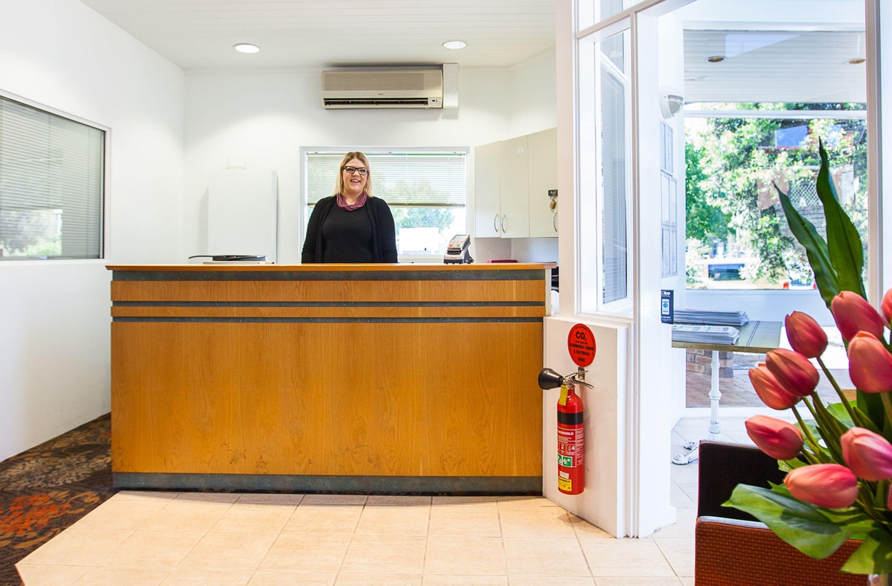 A reception desk with a fire extinguisher and a window with a view of greenery.