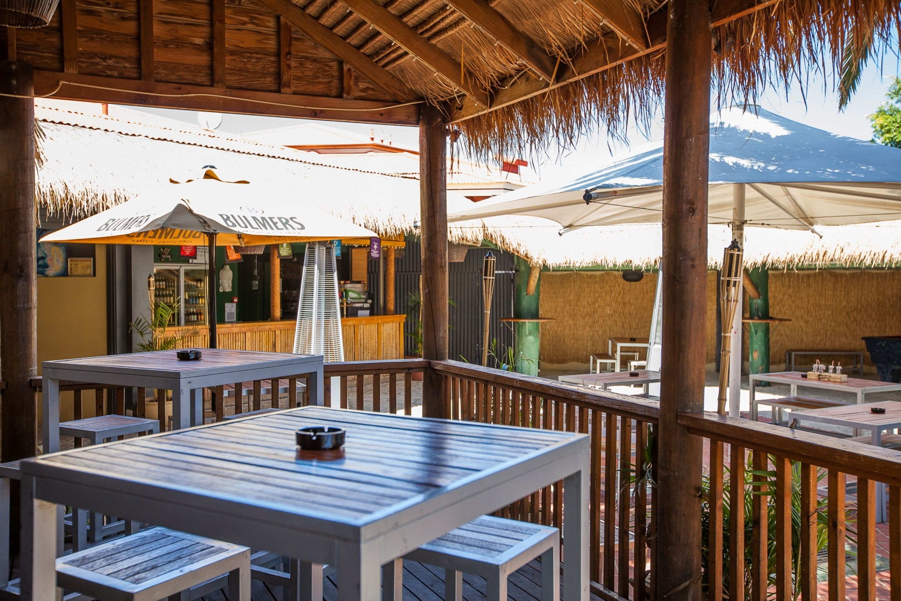 An outdoor patio area with wooden tables and benches, a thatched roof, and a view of a mountain.
