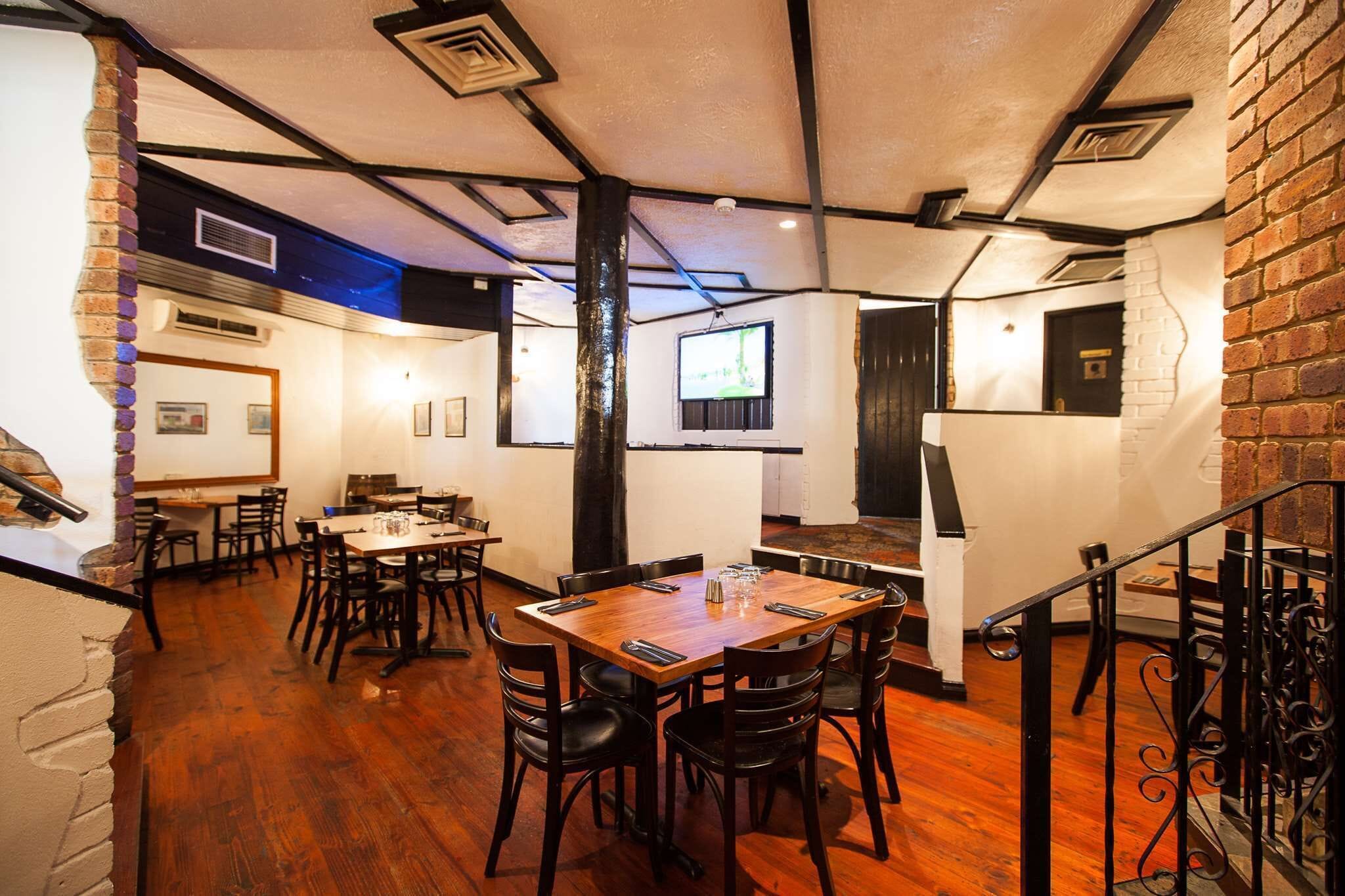 Un restaurante con mesas y sillas de madera, paredes de ladrillo y una escalera.