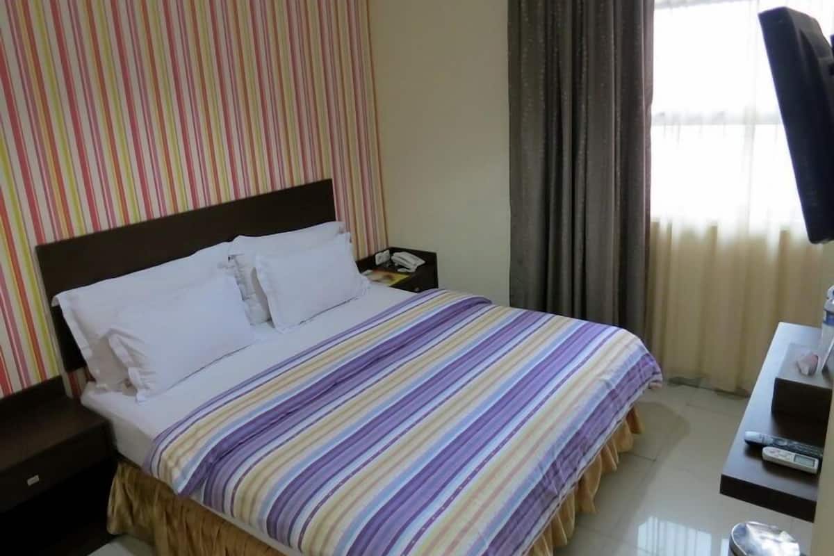 A hotel room with a bed, a nightstand, a desk with a chair, and a window with curtains.